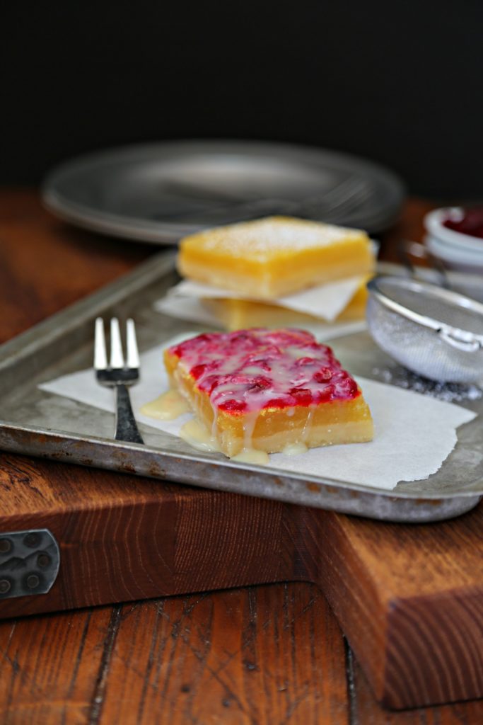 Lemon Cranberry Bars with White Chocolate Drizzle on baking sheet .with fork. Pewter plates in background.