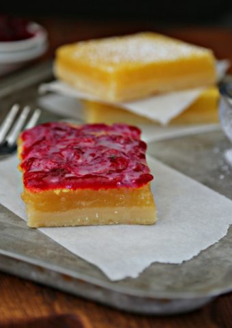 Lemon Cranberry Bars with White Chocolate Drizzle on baking sheet with fork and sieve with powdered sugar.