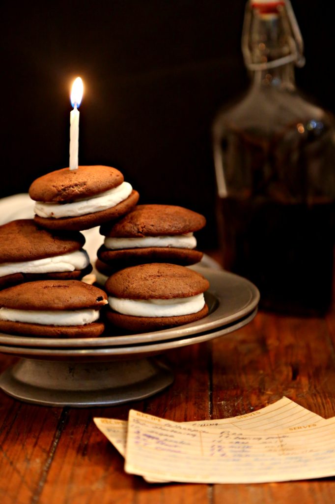 momma's old fashioned whoopies pies on a silver cake plate topped with a birthday candle bottle of vanilla extract and flour sifter
