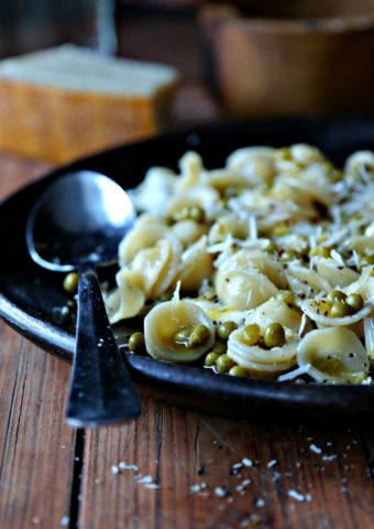 brown plate with silver spoon of orecchiette pasta with peas and parmesan