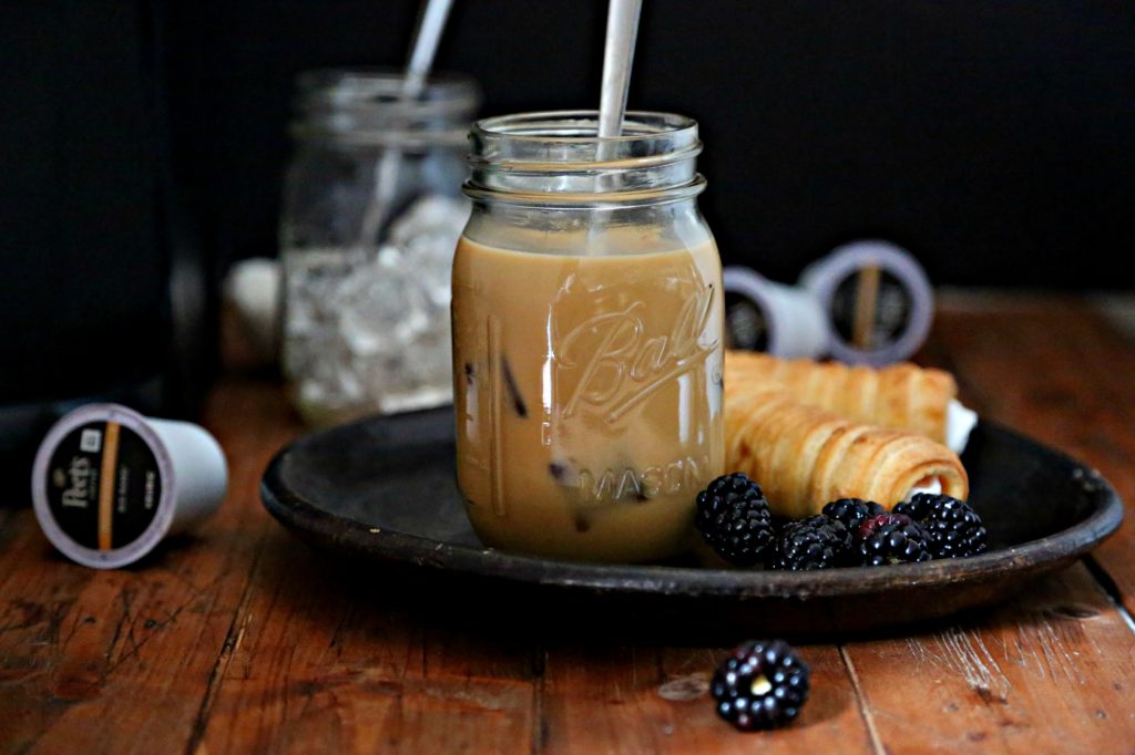 mason jar with iced coffee on plate with pastry and blackberries