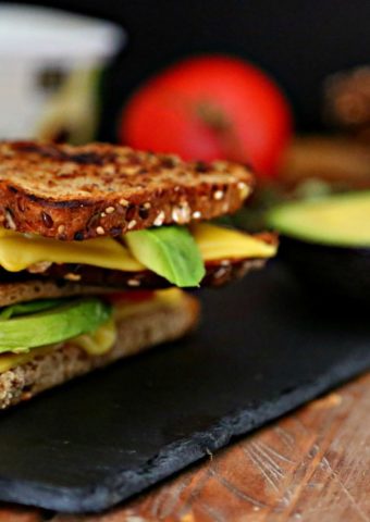 Avocado and Tomato Vegan Grilled Cheese on slate with tomato, butter and avocado surrounding.