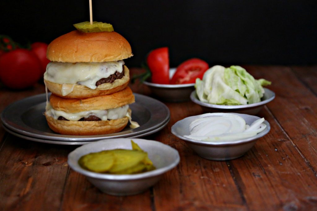 Two Cheeseburgers stacked on plate surrounded by toppings