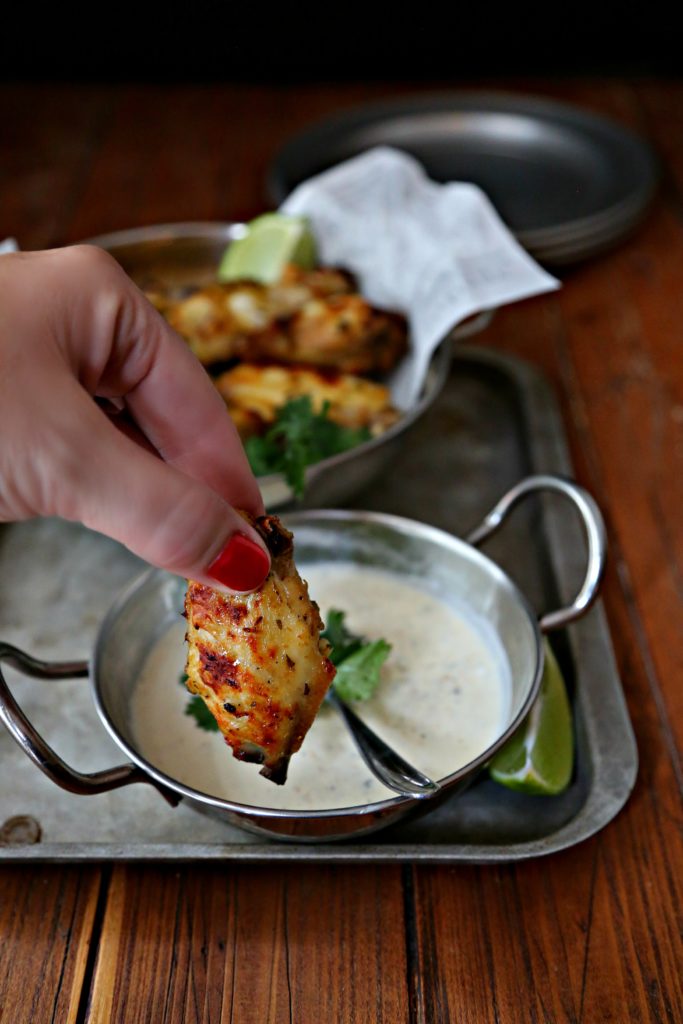 Salsa Verde Glazed Chicken Wings in silver bowl, hand dipping chicken wing into white sauce