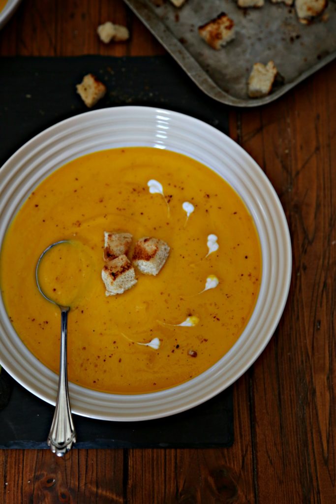 bowl of roasted butternut squash soup with croutons, spoon and garnish of creme fraiche