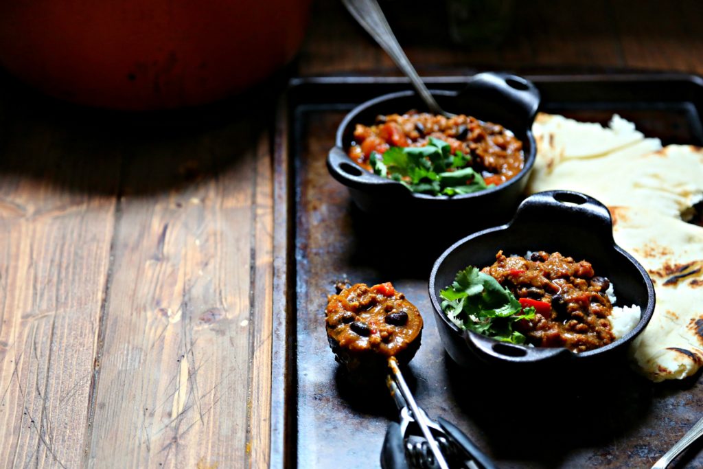 Turkey Black Bean Pumpkin Chili in small cast iron pots surrounded by naan bread and a scooper of chili