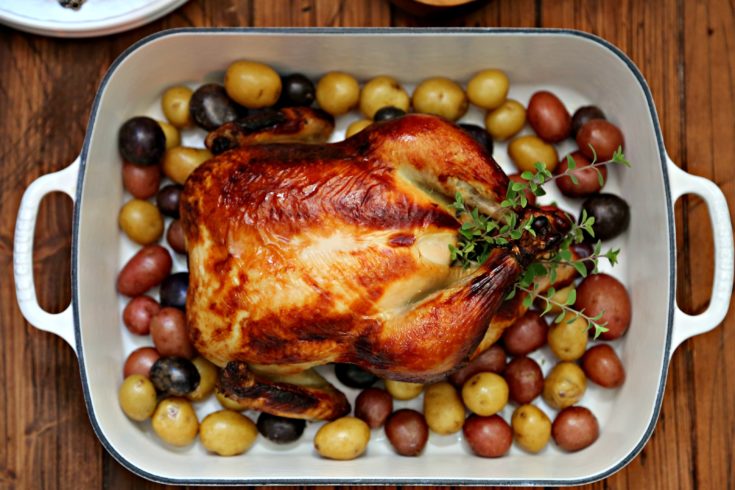 Buttermilk Brined Roast Chicken in roasting pan surrounded by new potatoes