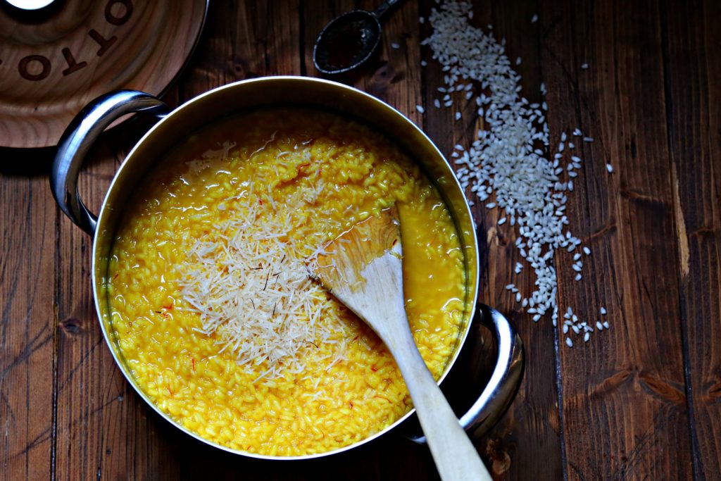 Pot of safron risotto with spoon of saffron and risotto scattered beside