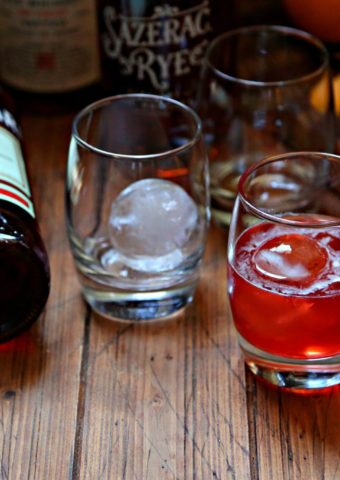 Boulevardier Cocktail with ice sphere and orange peel, extra glasses, bottle of campari and rye whiskey to side