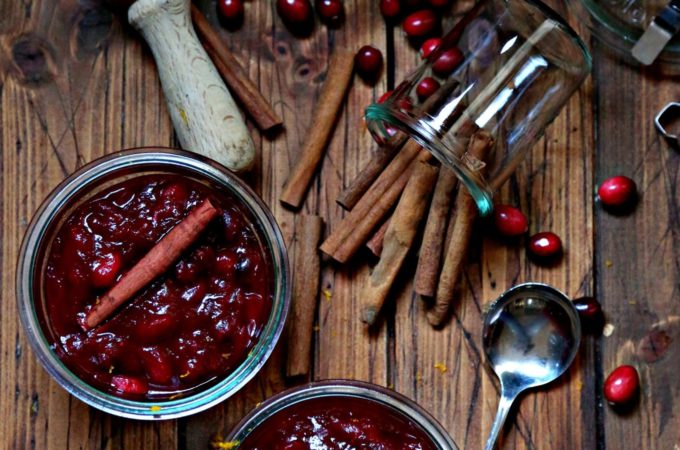 Cinnamon Orange Cranberry Sauce in glass jars surrounded by cinnamon sticks and fresh cranberries