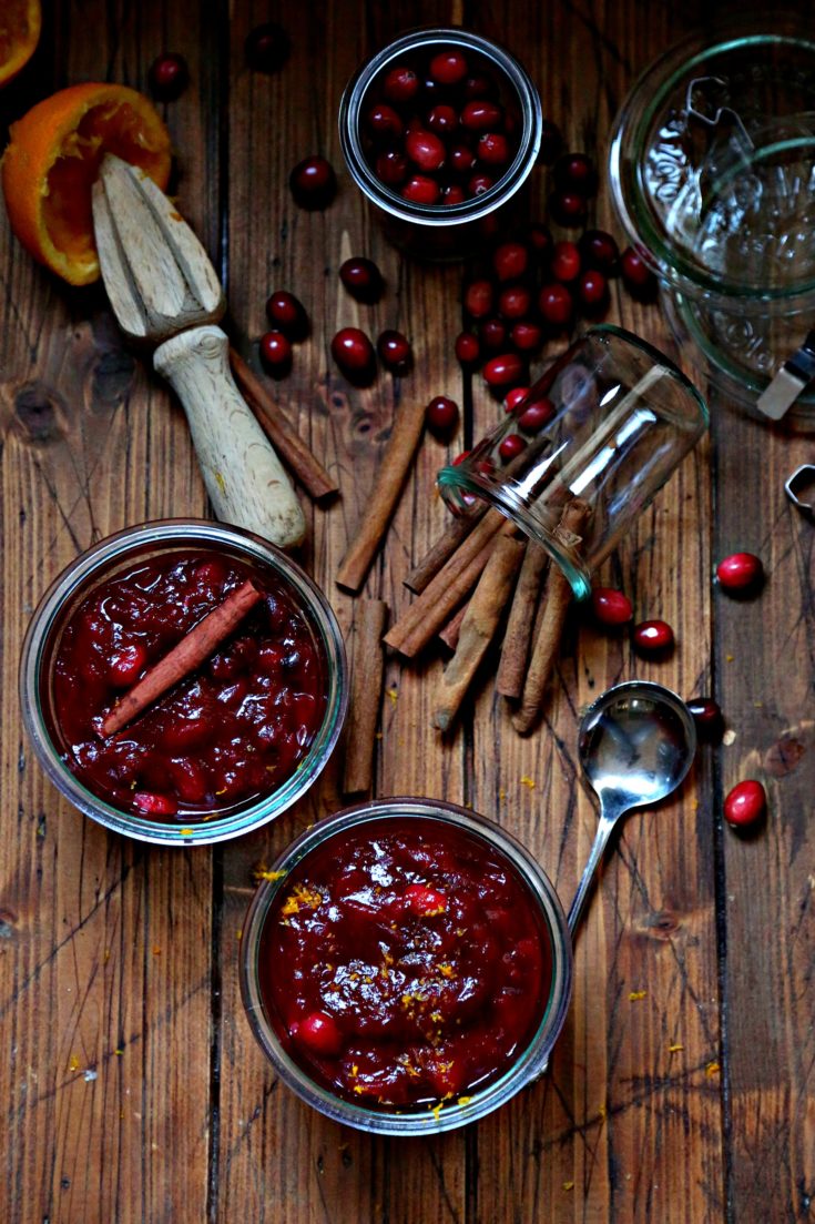 Cinnamon Orange Cranberry Sauce in glass jars surrounded by cinnamon sticks and fresh cranberries