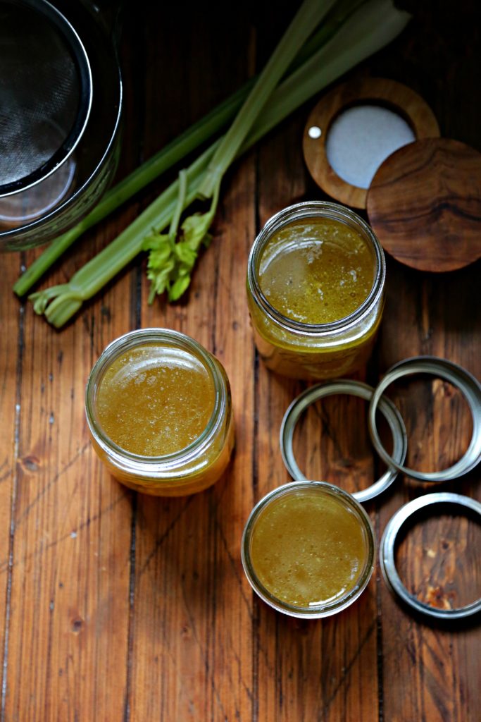 Easy Instant Pot Chicken Stock in jars with celery, salt and strainer to side 