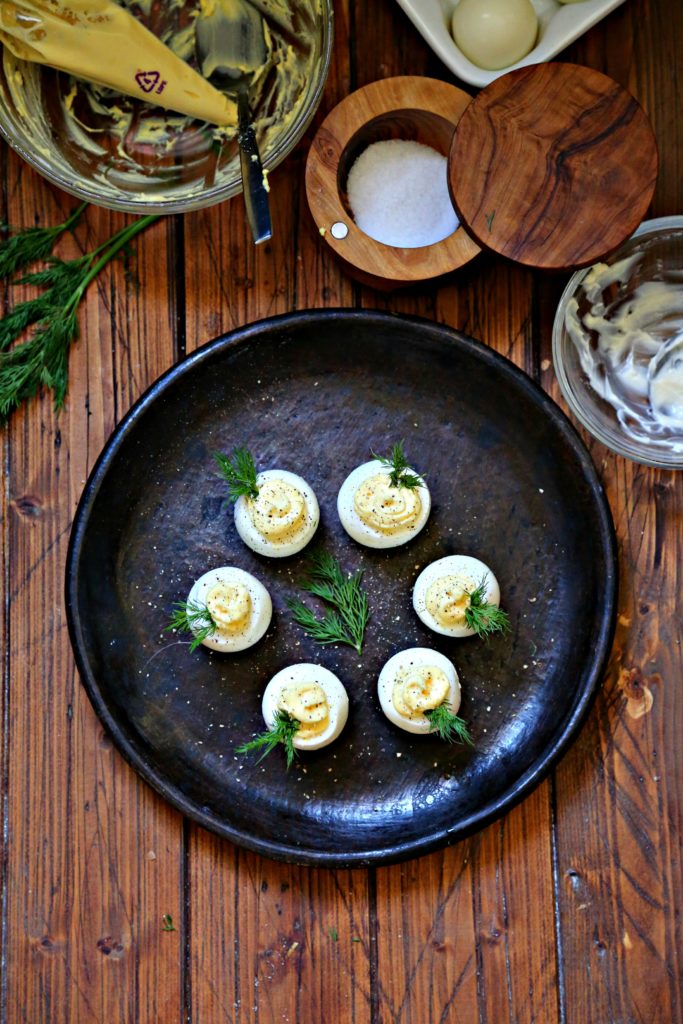 Deviled Eggs on a brown plate surrounded by bowl of filling mixture, salt cellar