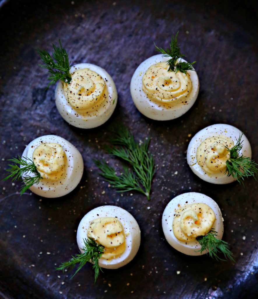 Deviled eggs garnished with dill on brown plate 