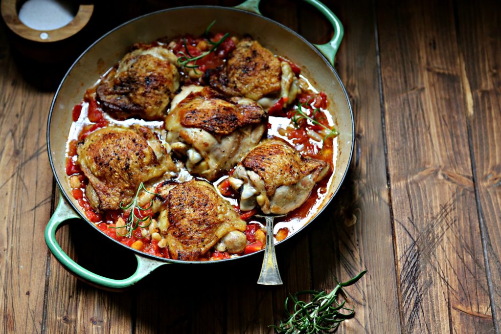 Skillet Chicken Thighs with Fire-Roasted Tomatoes and White Beans in green skillet with spoon and rosemary to side