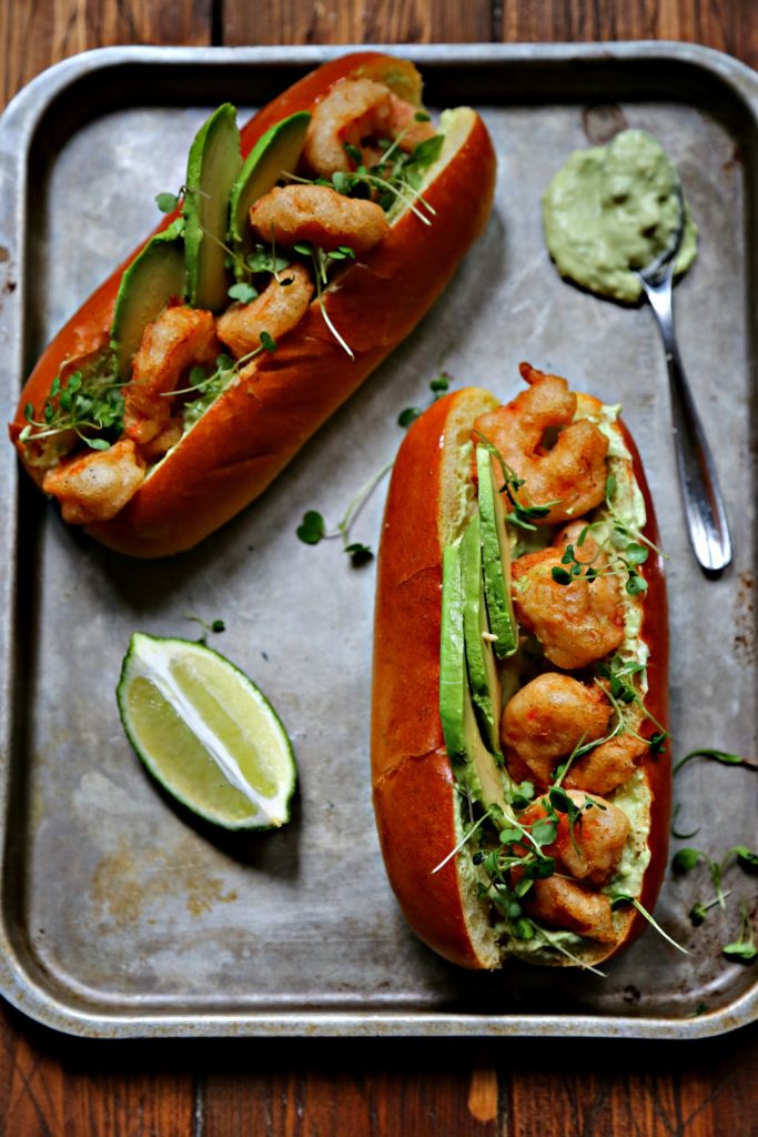 Spicy Shrimp Po Boy with Avocado Crema on baking sheet with lime wedge and spoon of avocado crema