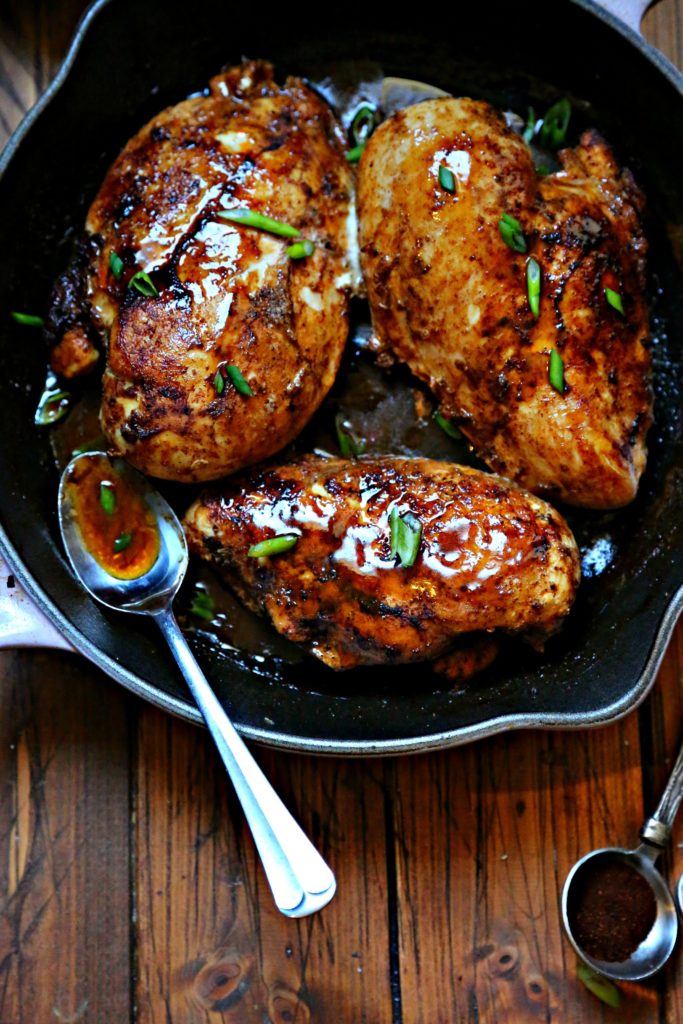 Spicy Skillet Chicken breasts with Pan Sauce in cast iron skillet with spoon in skillet. Measuring spoon with spice to side.