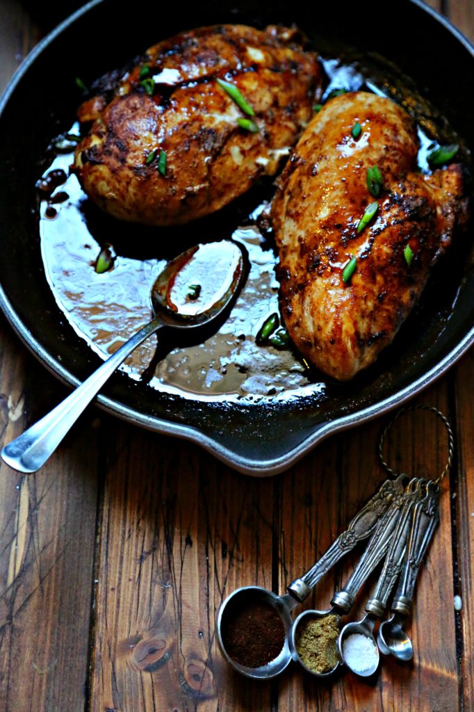 Spicy Skillet Chicken with Pan Sauce in cast iron skillet with spoon and measuring spoons with spice to side