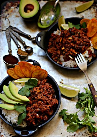 2 small cast iron skillets filled with rice, picadillo, avocado, cilantro, plaintain chips. Measuring spoons with spices behind.