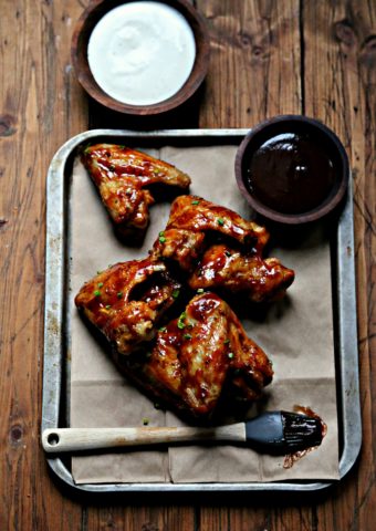 Chicken Wings on baking sheet with silicon brush and bowl of bbq sauce. Bowl of ranch behind.