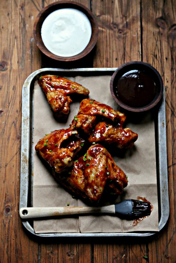 Chicken Wings on baking sheet with silicon brush and bowl of bbq sauce. Bowl of ranch behind. 