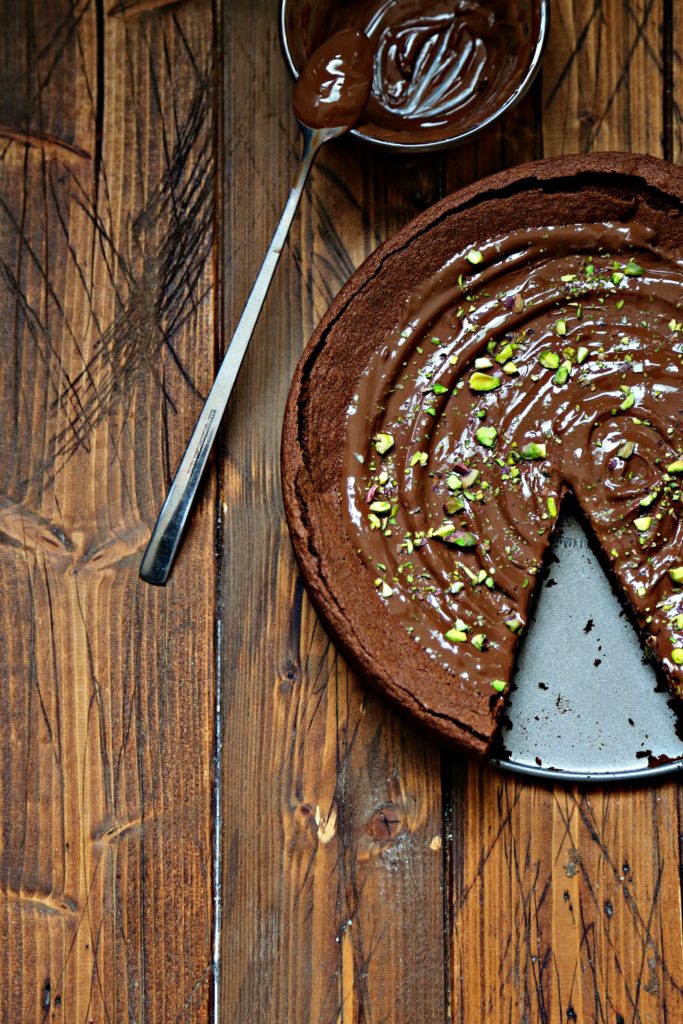 Chocolate Cake with Nutella Frosting with piece missing. Small glass bowl of Nutella with spoon behind.
