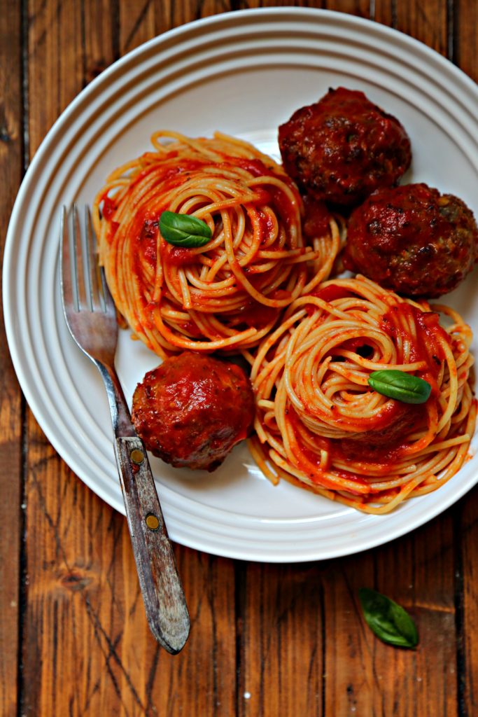 spaghetti and meatballs topped with basil in white bowl with fork.