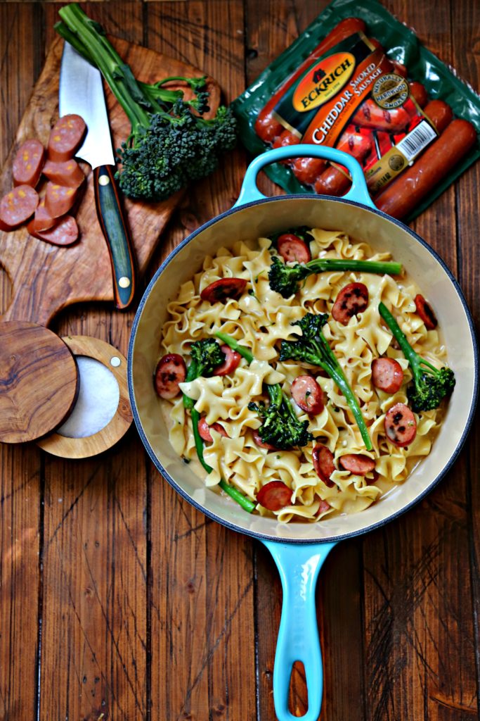 Pot of Pasta with broccoli and sausage. Cutting board with slice sausage, brocoli and package of sausage behind.