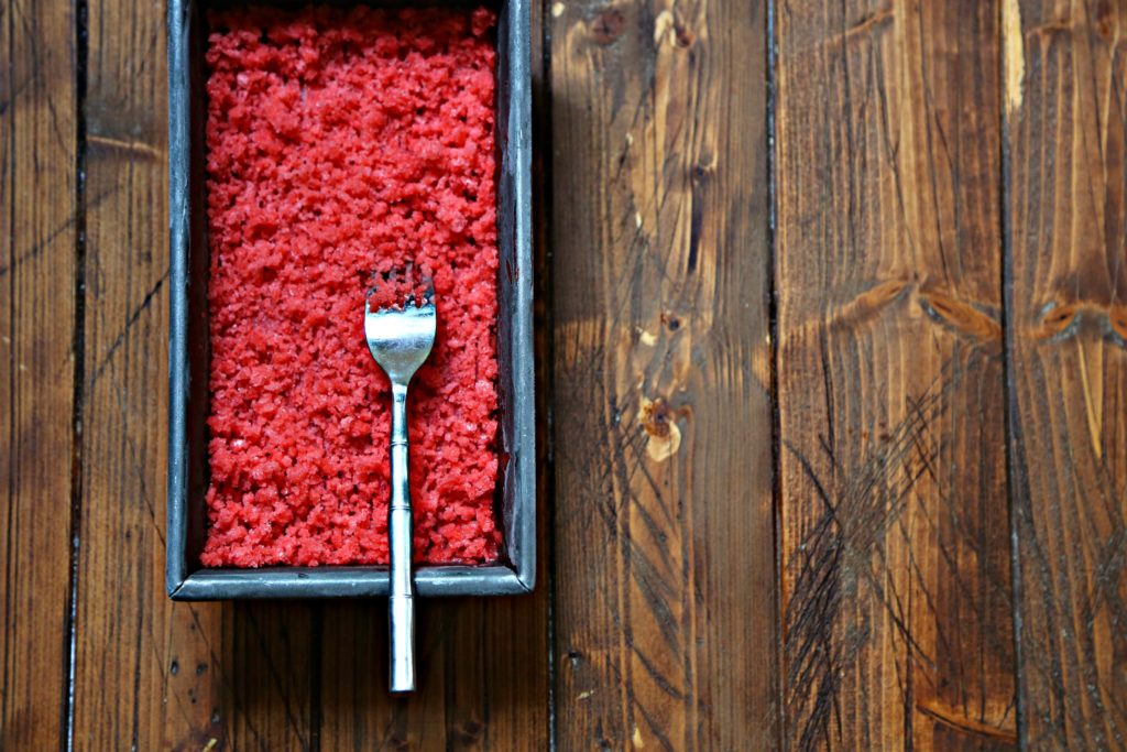 strawberry granita in metal loaf pan with fork.