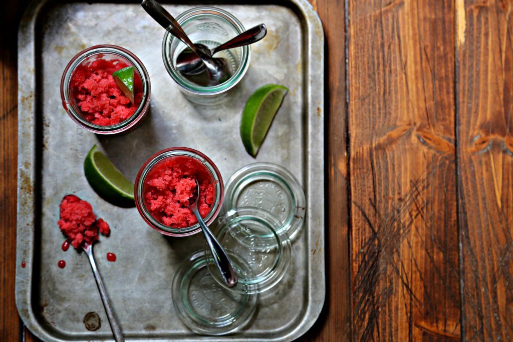 strawberry granitas in glass jars with spoons. Lime wedges to side.