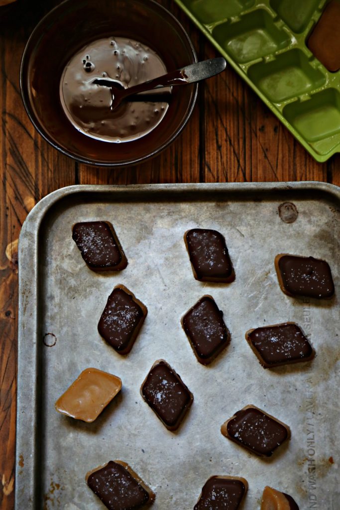 chocolate dipped peanut butter fat bombs on baking sheet. Bowl of chocolate with spoon behind.