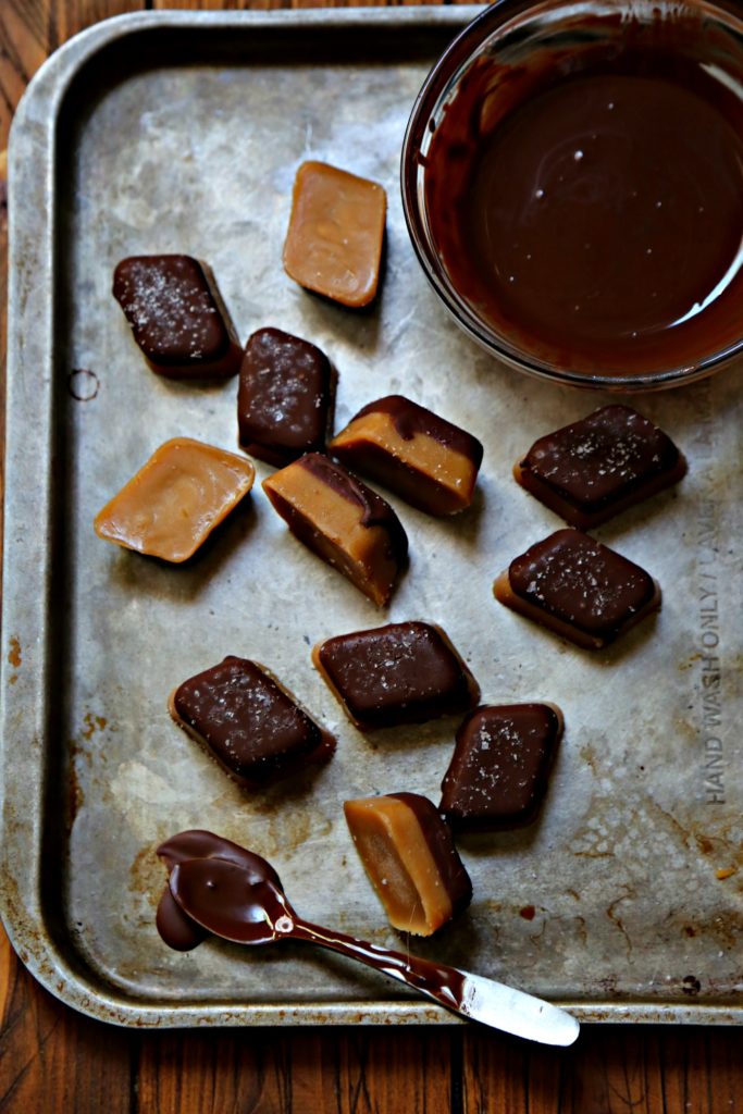 chocolate dipped peanut butter fat bombs scattered on baking sheet. Small bowl of melted chocolate on tray. 
