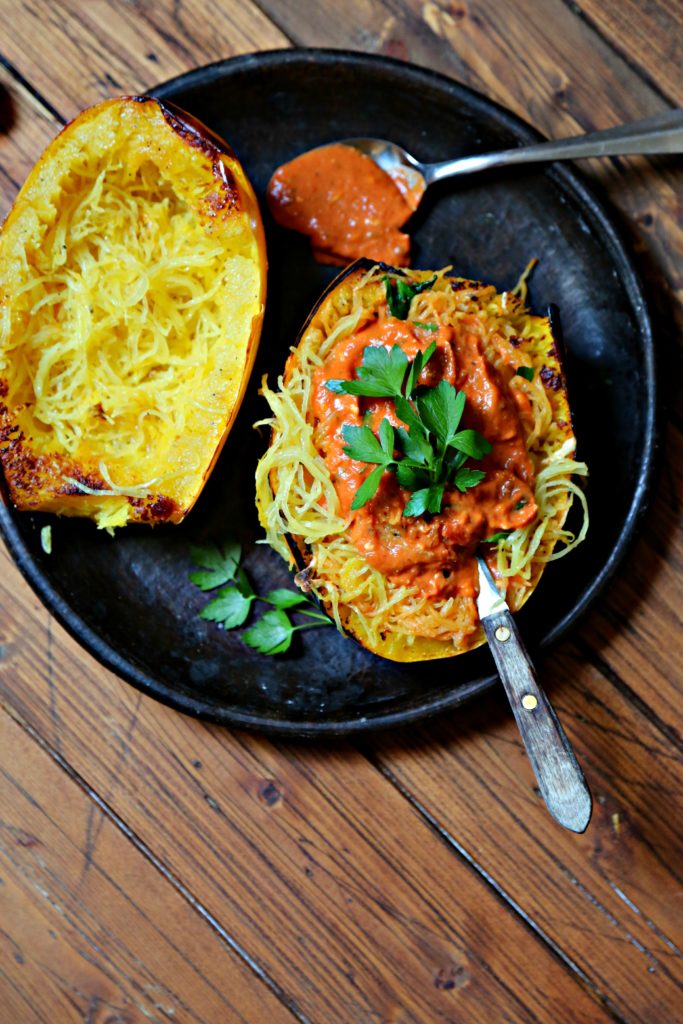 roasted spaghetti squash on brown plate with spoon of sauce.