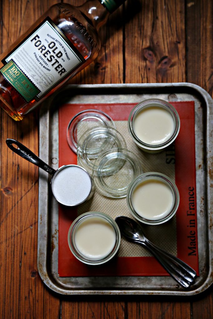 small glass jars filled with whiskey panna cotta on baking sheet with bottle of rye. 