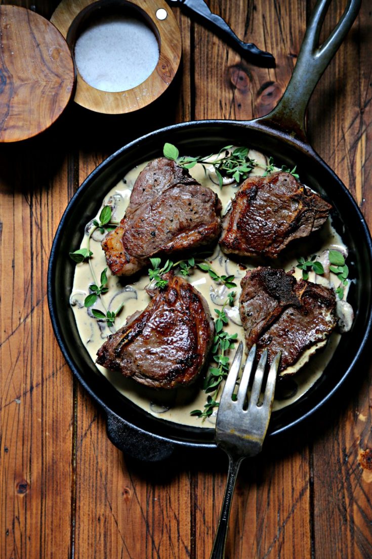 Lamb chops in mustard sauce in cast iron skillet with serving fork.
