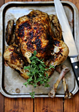 Whole roasted chicken on baking sheet with knife.