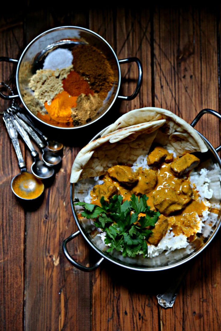 Butter chicken in silver bowl with rice. Silver bowl with spices behind.