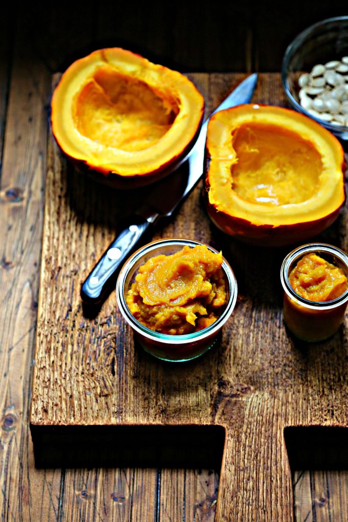 Pumpkin puree in glass jars on cutting board. Knife and pumpkin halves behind.