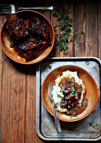 Coca Cola Braised Short Ribs in shallow brown bowl. Second bowl filled with mashed potatoes and topped with shredded ribs.