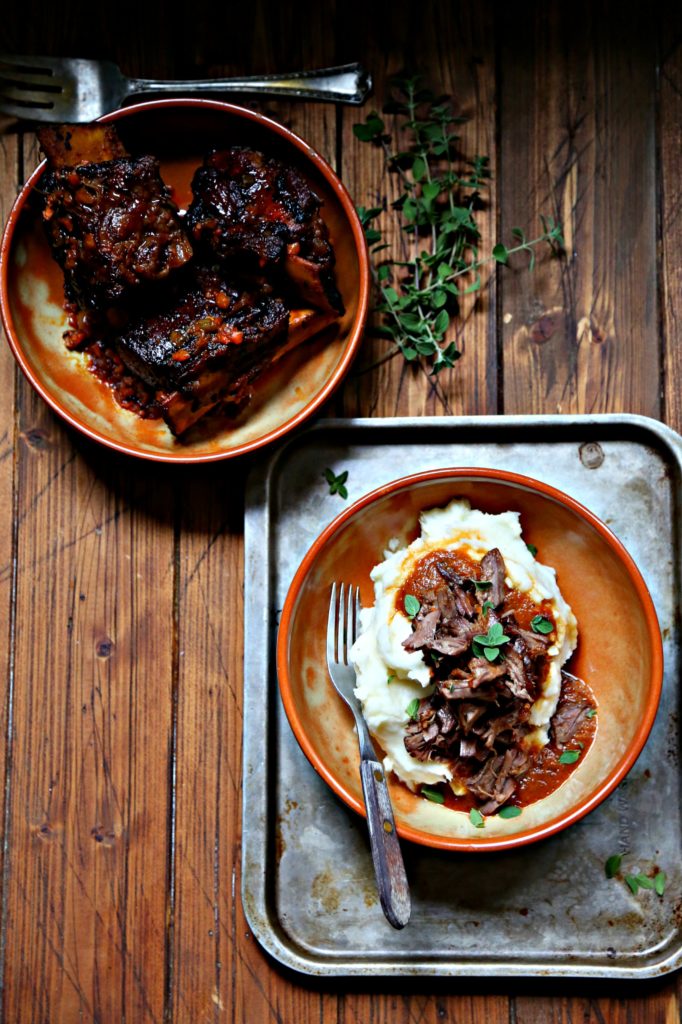 Coca Cola Braised Short Ribs in shallow brown bowl. Second bowl filled with mashed potatoes and topped with shredded ribs.