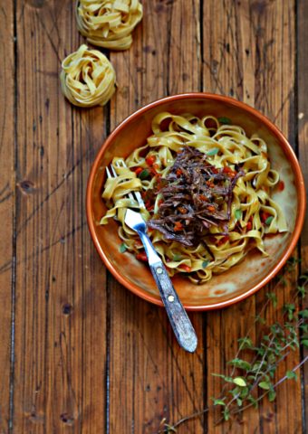 Bowl of pasta with shredded short ribs. Dried pasta nests in background.