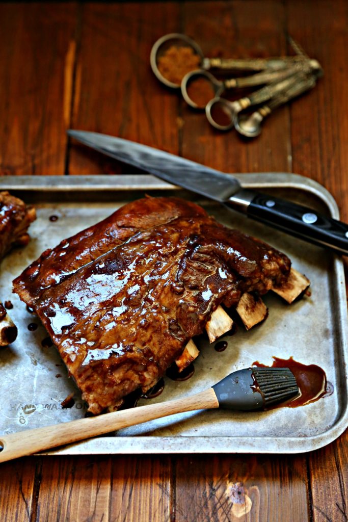 half rack of ribs on baking sheet with knife and silicone brush.