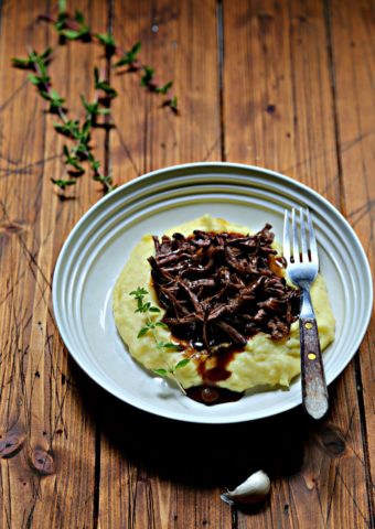 mashed potatoes, shredded short ribs and gravy in white bowl with fork. Fresh thyme in background.
