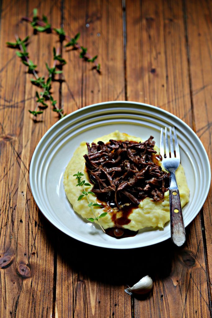 mashed potatoes, shredded short ribs and gravy in white bowl with fork. Fresh thyme in background. 