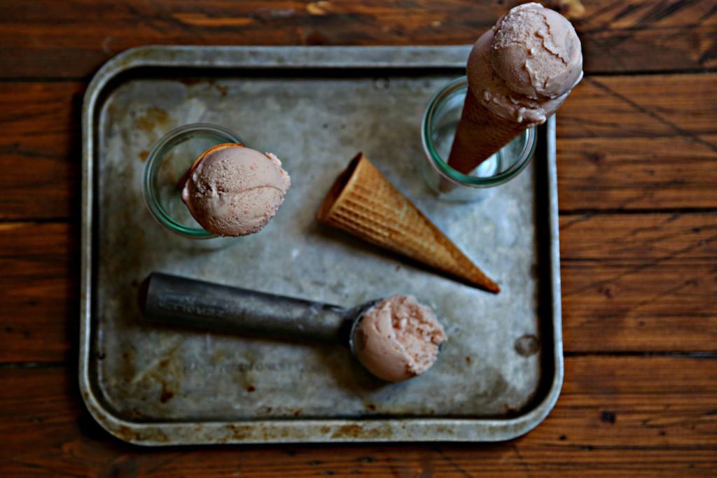 Baking sheet with scoop of Strawberry Ice Cream. Empty sugar cone. Ice cream cone standing in small glass jar.