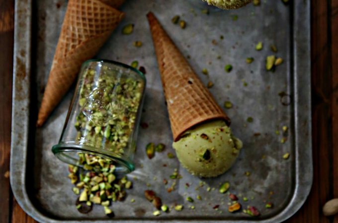 baking sheet with stack of ice cream cones. Small glass of crushed pistachios on its side. Ice cream cone standing in small glass jar.