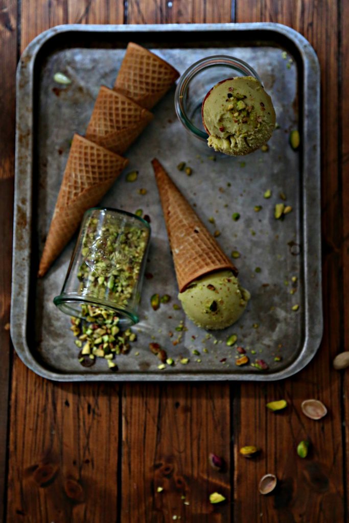 baking sheet with stack of ice cream cones. Small glass of crushed pistachios on its side. Ice cream cone standing in small glass jar. 