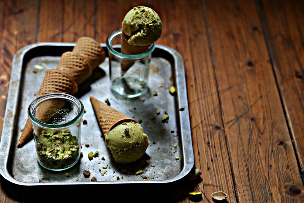 baking sheet with ice cream cones laying on side. Small glass jar of crushed pistachios. Ice cream cone standing in glass jar. 