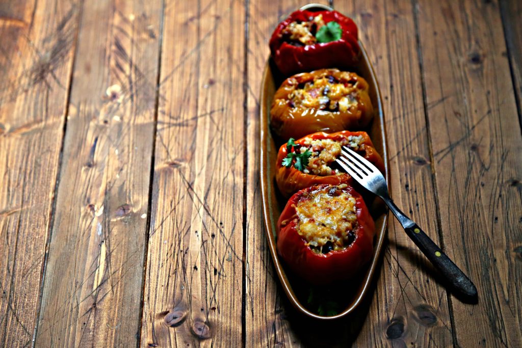 4 rice stuffed bell peppers on brown oblong tray. Fork piercing one pepper. 
