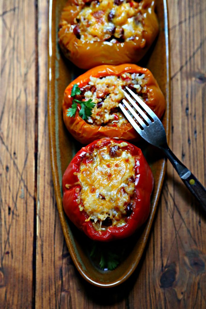 close up of 3 stuffed bell peppers on brown oblong tray. Fork poking into middle bell pepper. 